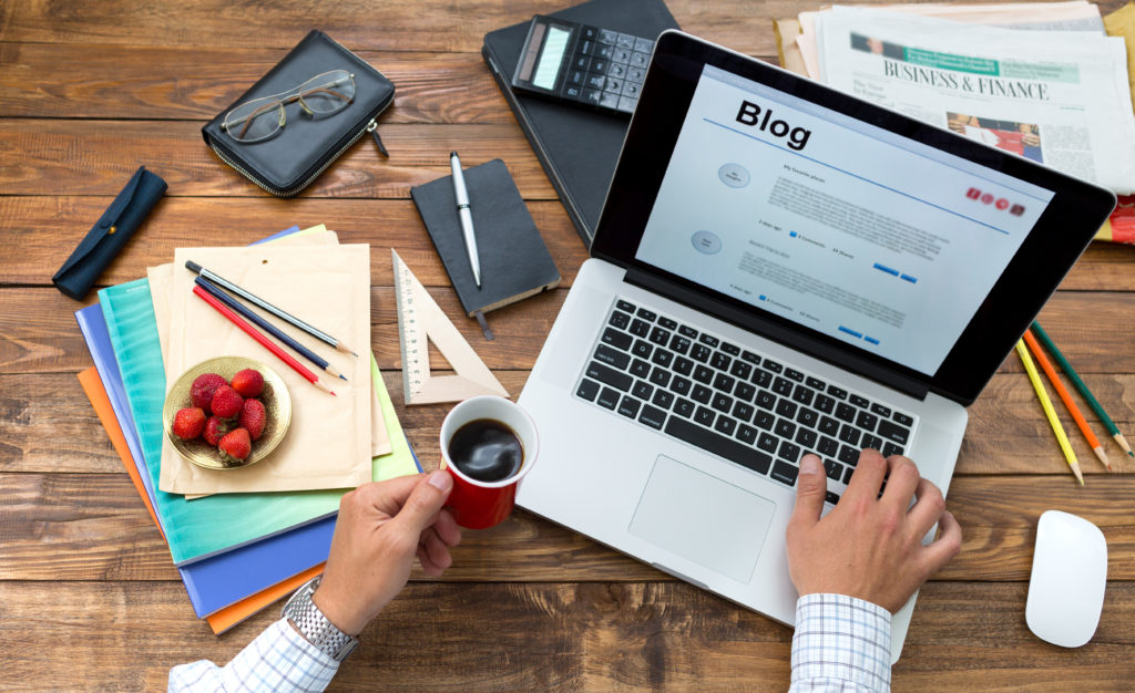 business owner blogging on laptop with notes and cup of coffee